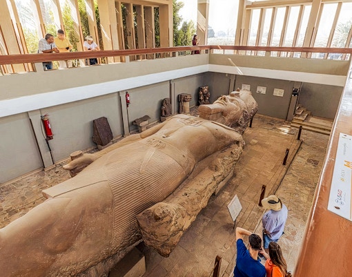 Colossal statue of Ramses II in Cairo museum with visitors observing.