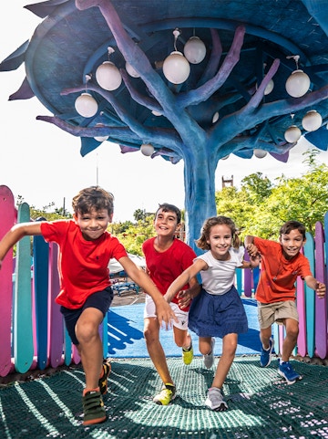 Children playing under a colorful tree structure at Isla Mágica theme park.
