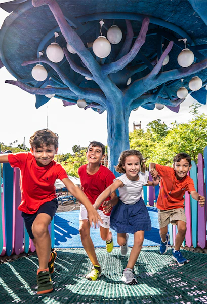 Children playing under a colorful tree structure at Isla Mágica theme park.