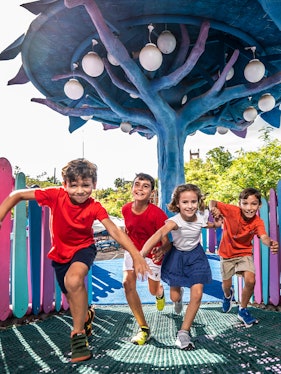 Children playing under a colorful tree structure at Isla Mágica theme park.