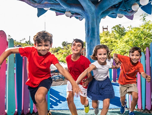 Children playing under a colorful tree structure at Isla Mágica theme park.