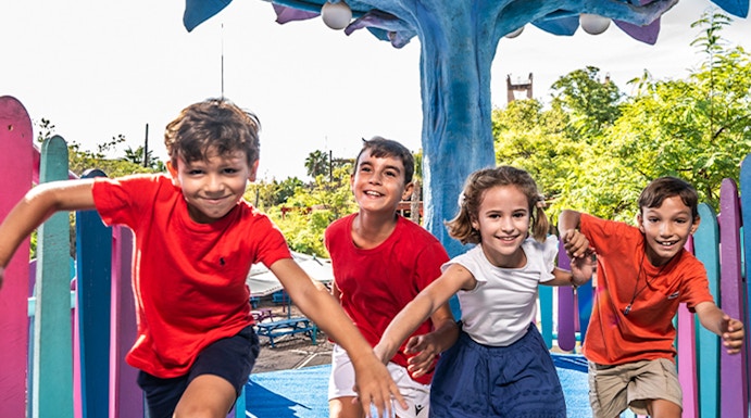Children playing under a colorful tree structure at Isla Mágica theme park.