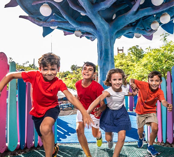 Children playing under a colorful tree structure at Isla Mágica theme park.