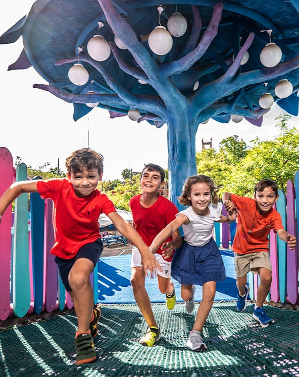 Children playing under a colorful tree structure at Isla Mágica theme park.