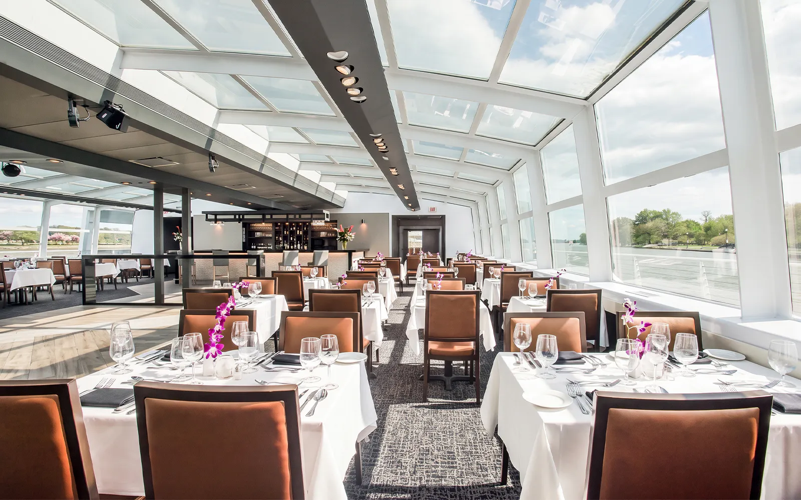 Dining hall set for Premier Bottomless Mimosa Brunch Cruise in Washington DC with river views.