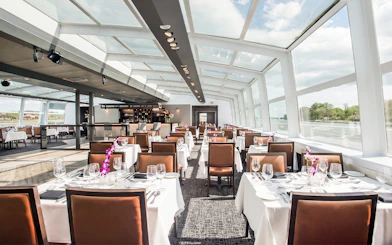 Dining hall set for Premier Bottomless Mimosa Brunch Cruise in Washington DC with river views.