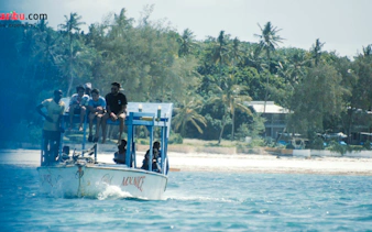Glass-bottom boat with tourists near Robinson Island, Diani Beach, surrounded by palm trees.