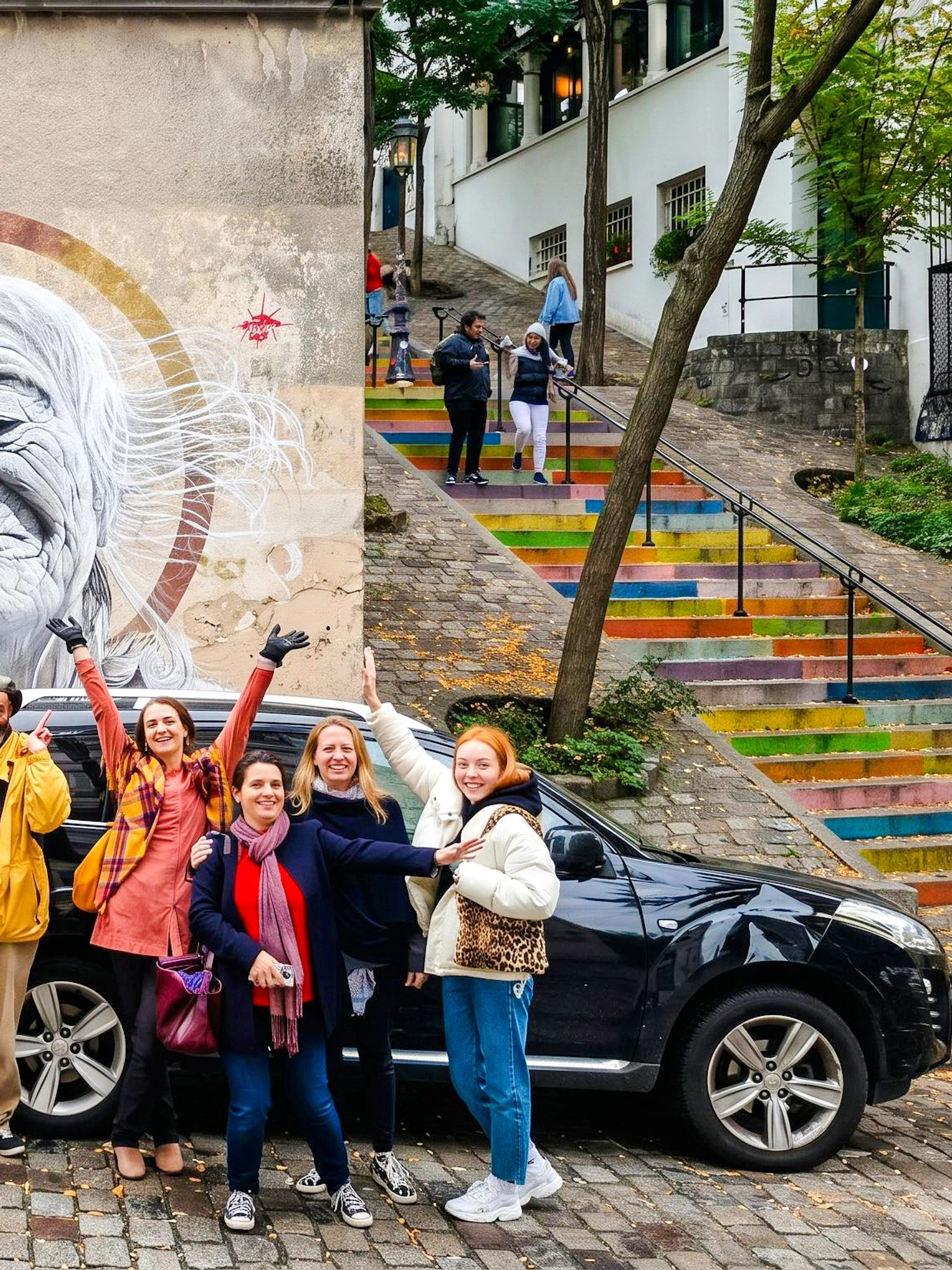 Group posing by Montmartre street art mural, colorful stairs in background, Paris tour.