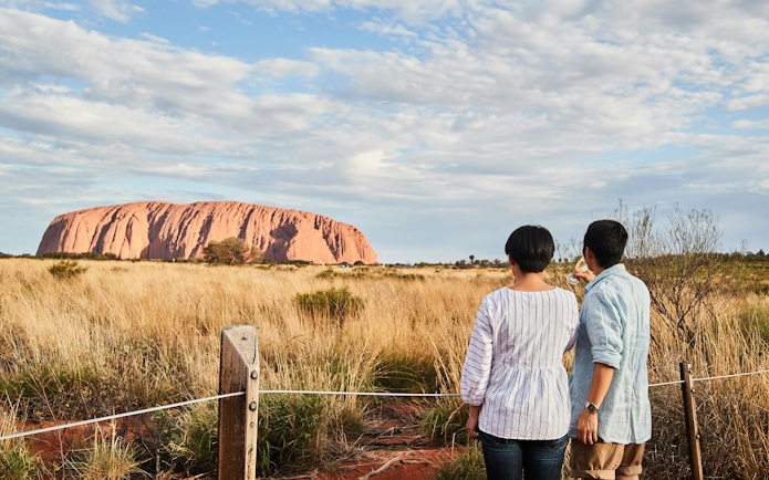 Couple enjoying sunset view of Uluru with sparkling wine in Australia.