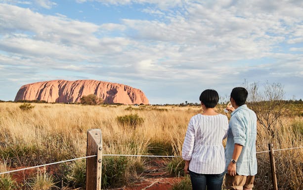 Couple enjoying sunset view of Uluru with sparkling wine in Australia.