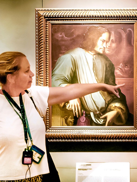 Guide explaining Renaissance painting to group at Uffizi Gallery.