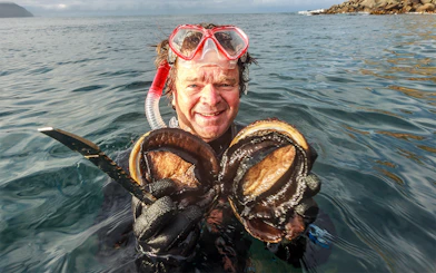 Snorkeler holding fresh abalone in Tasmanian waters during Seafood Seduction tour.