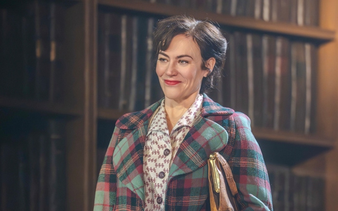 Stage performance of Shadowlands in Westend, actor in plaid coat with bookshelves in background.