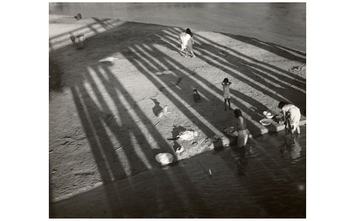 Women washing clothes by a river, shadows cast by a bridge, part of the National Gallery of Victoria exhibition.