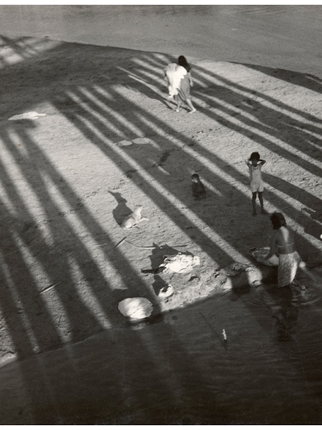Women washing clothes by a river, shadows cast by a bridge, part of the National Gallery of Victoria exhibition.