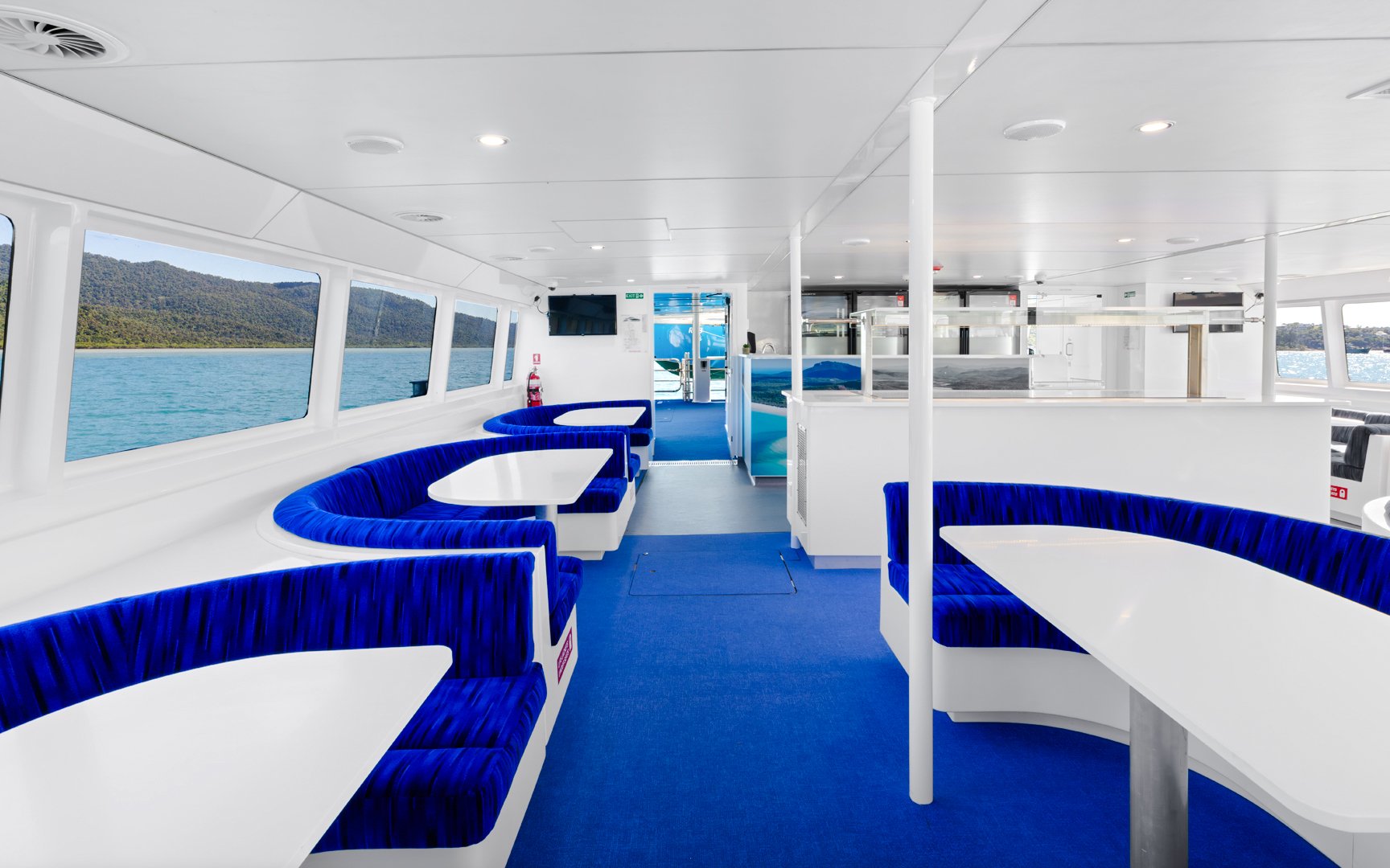 Interior of a cruise boat with blue seating, large windows showing ocean views near Airlie Beach.