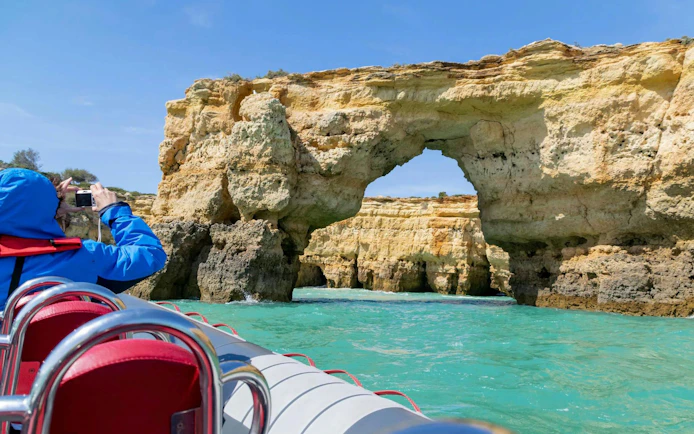 Boat approaching Benagil Cave rock formation in Portimão, with a person taking photos.
