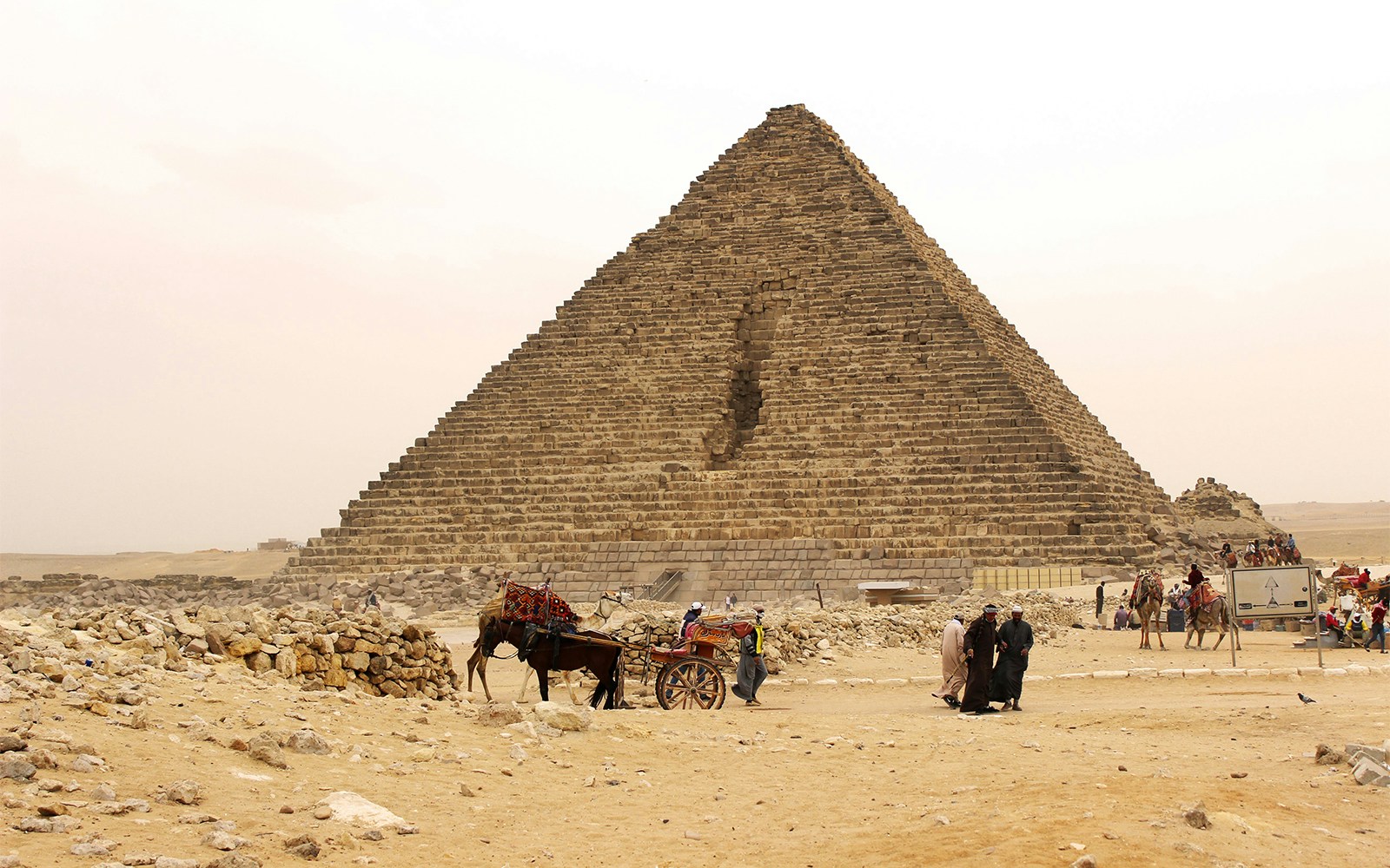 Pyramid of Menkaure in Giza with tourists and camels nearby.