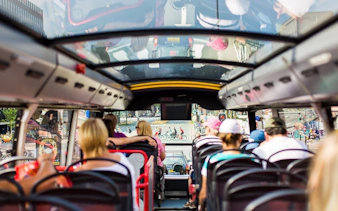 Passengers on Amsterdam hop-on hop-off bus tour with city view through glass roof.