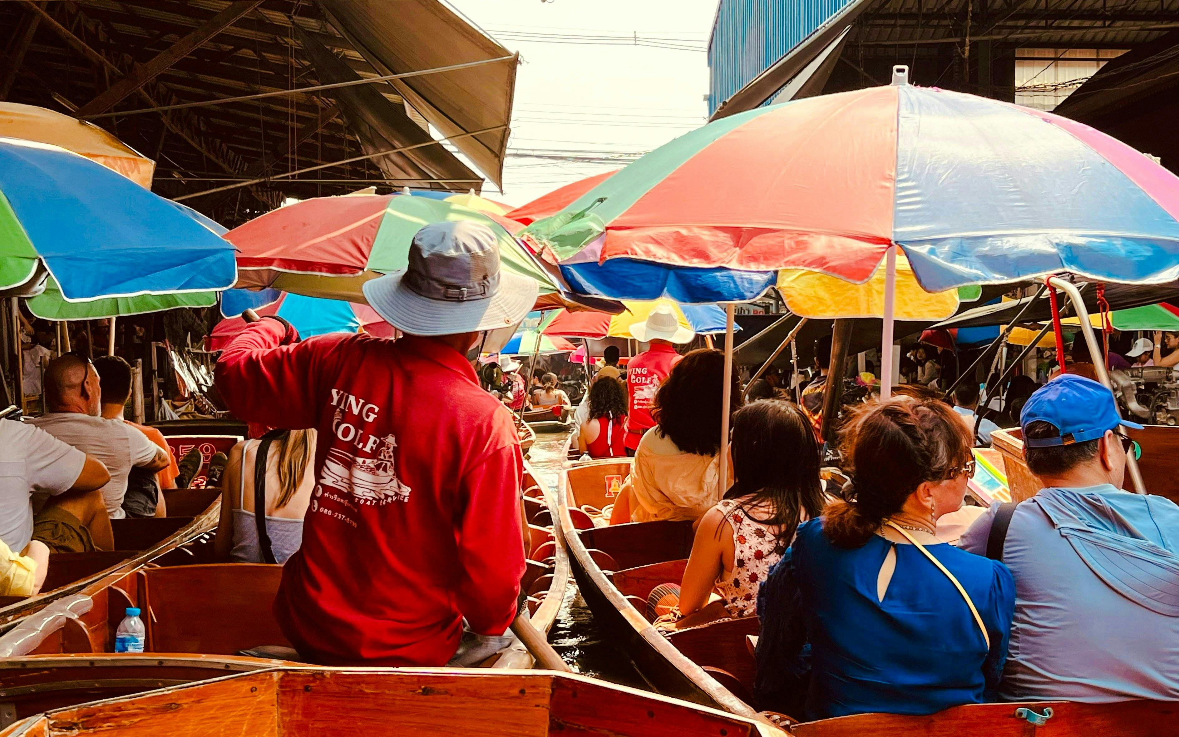 Tourists on boats at Damnoen Saduak Floating Market with colorful umbrellas.