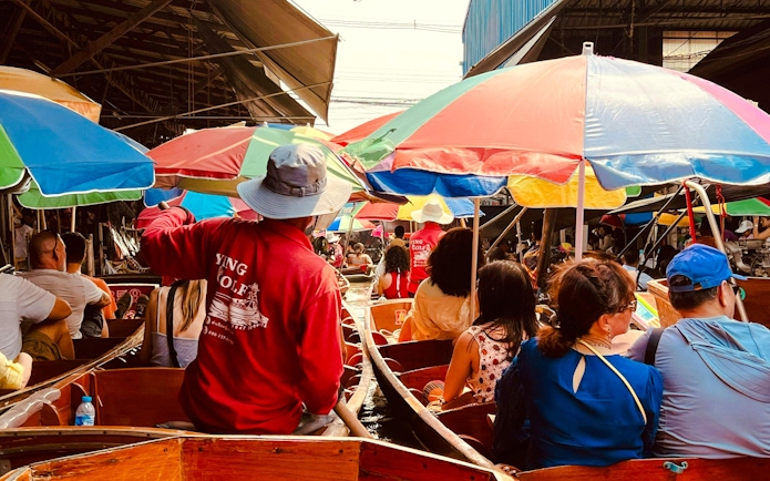 Tourists on boats at Damnoen Saduak Floating Market with colorful umbrellas.