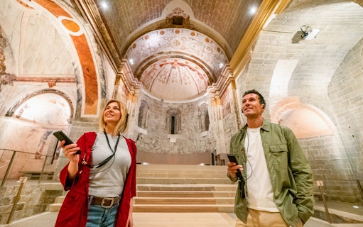 Visitors exploring the medieval architecture of Món Sant Benet with audio guides.