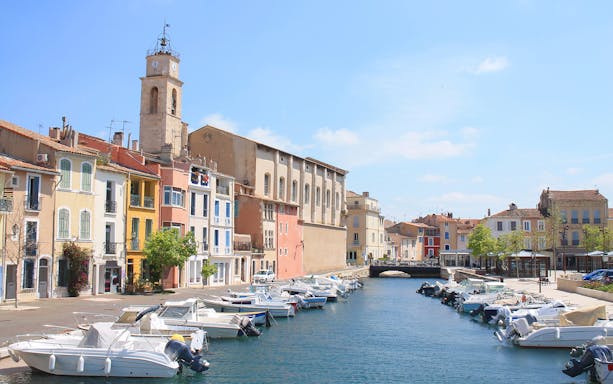 Boats docked along a canal with colorful buildings in Marseille's sea district.