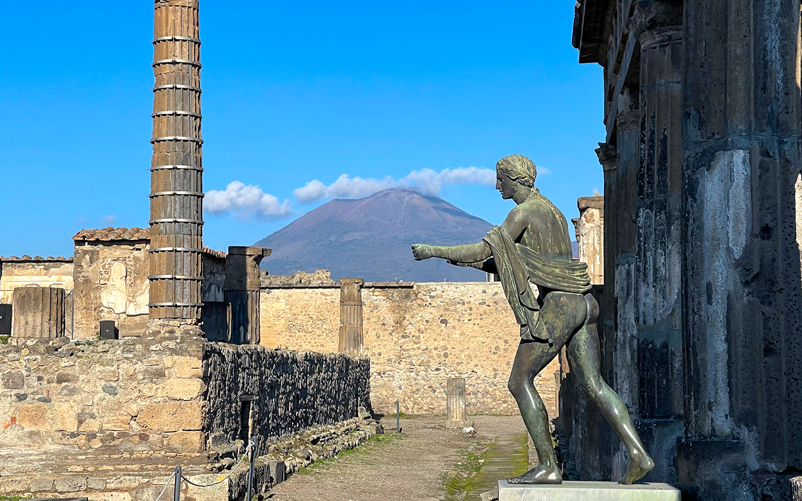 Statue in Pompeii ruins with Mount Vesuvius in the background.