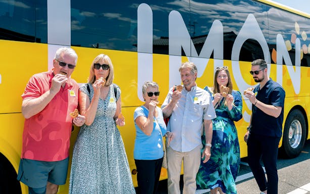 Tour group enjoying snacks in front of a yellow tour bus on the Kyoto Day Tour from Osaka Namba.
