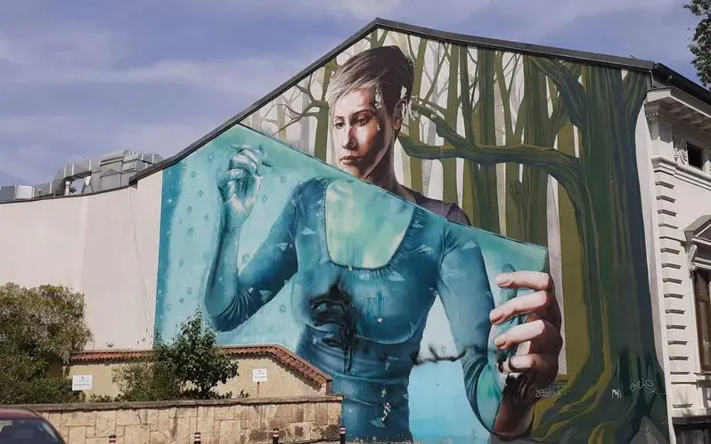 Mural of a woman in a forest setting on a building in Bucharest, part of the Spy Game city exploration.