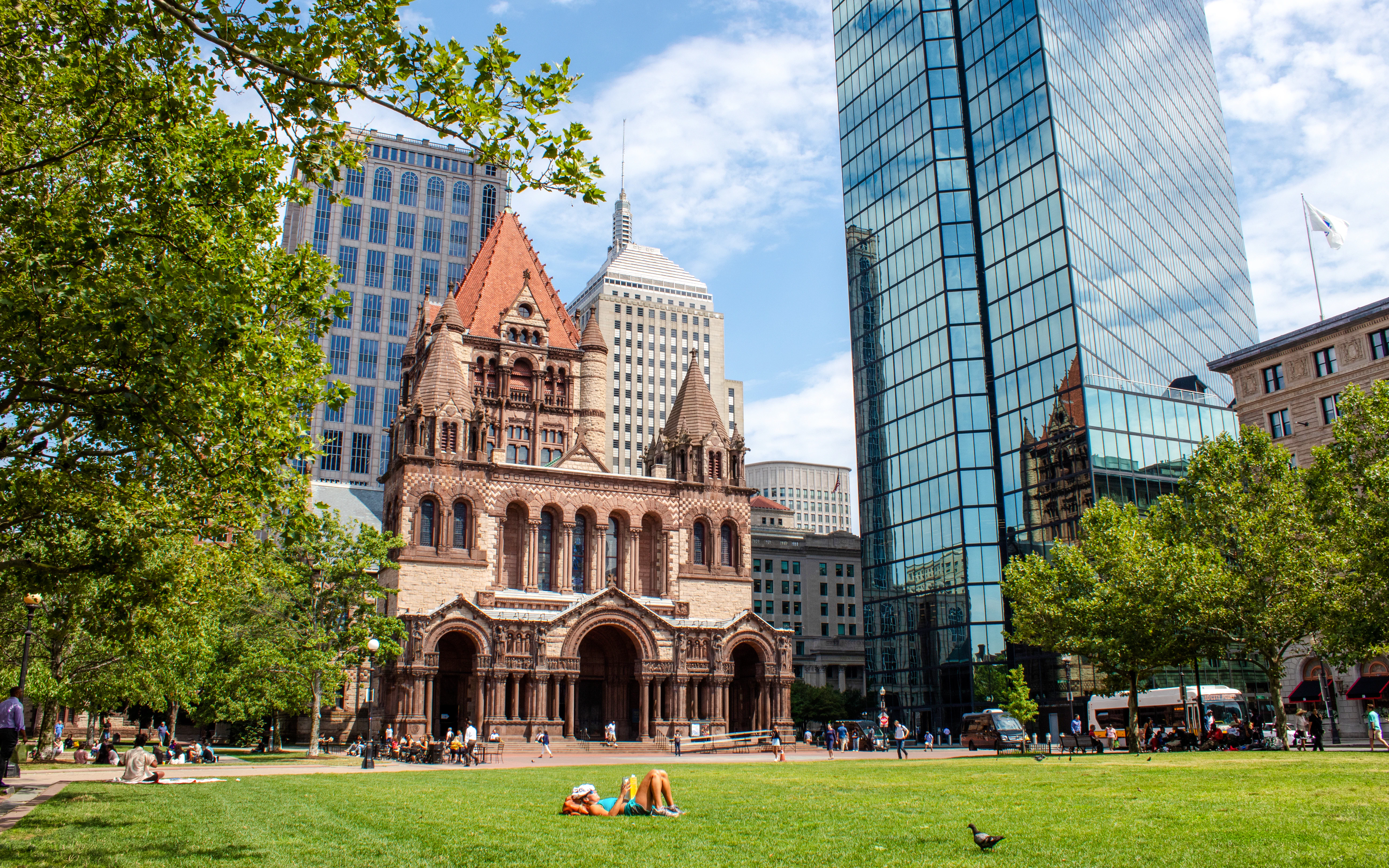 Trinity Church and Hancock Tower in Copley Square, Boston, with people relaxing on the grass.
