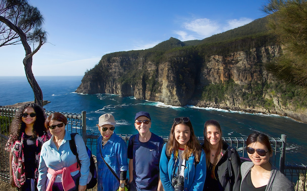 Group of tourists at Tasman Peninsula cliff lookout, Port Arthur, with ocean and cliffs in background.