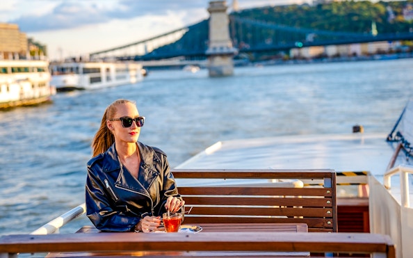 Guest enjoying river view on Elegant Premium Sightseeing Cruise with bridge in background.