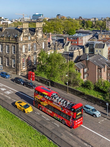 Open-top tour bus on a street in Edinburgh with historic buildings in the background.