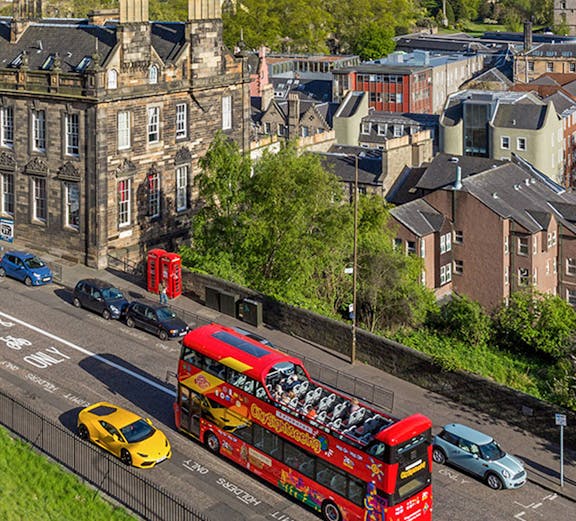 Open-top tour bus on a street in Edinburgh with historic buildings in the background.