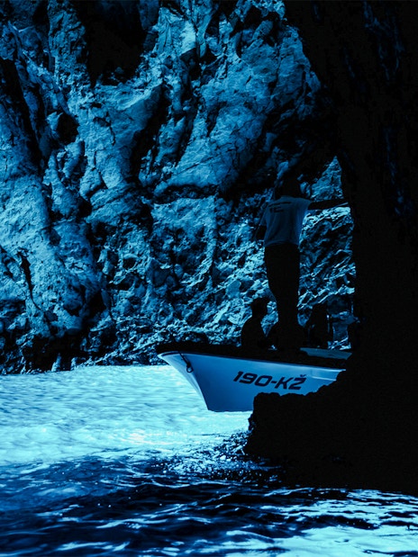 Boat entering the illuminated Blue Cave with rocky walls.