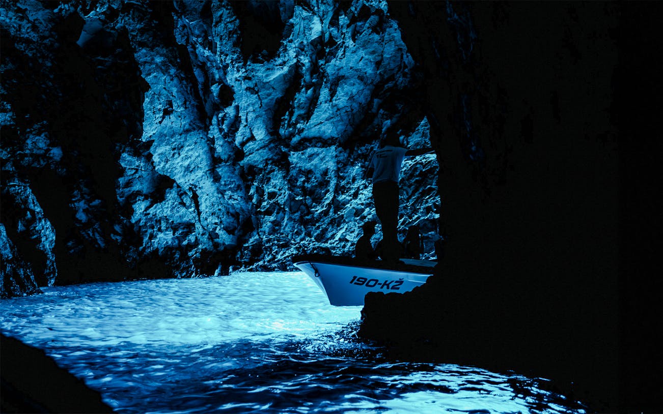 Boat entering the illuminated Blue Cave with rocky walls.