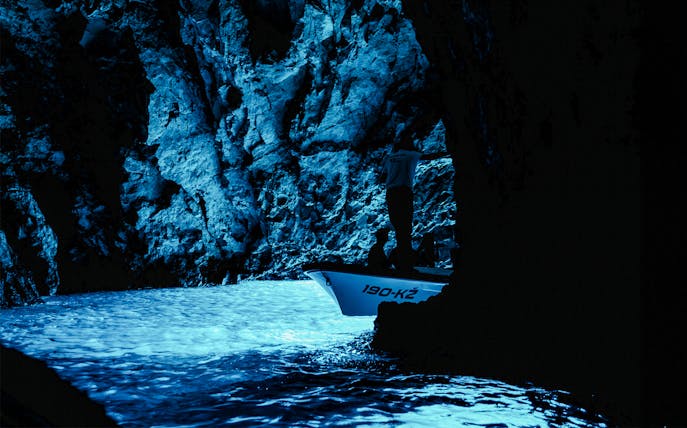 Boat entering the illuminated Blue Cave with rocky walls.