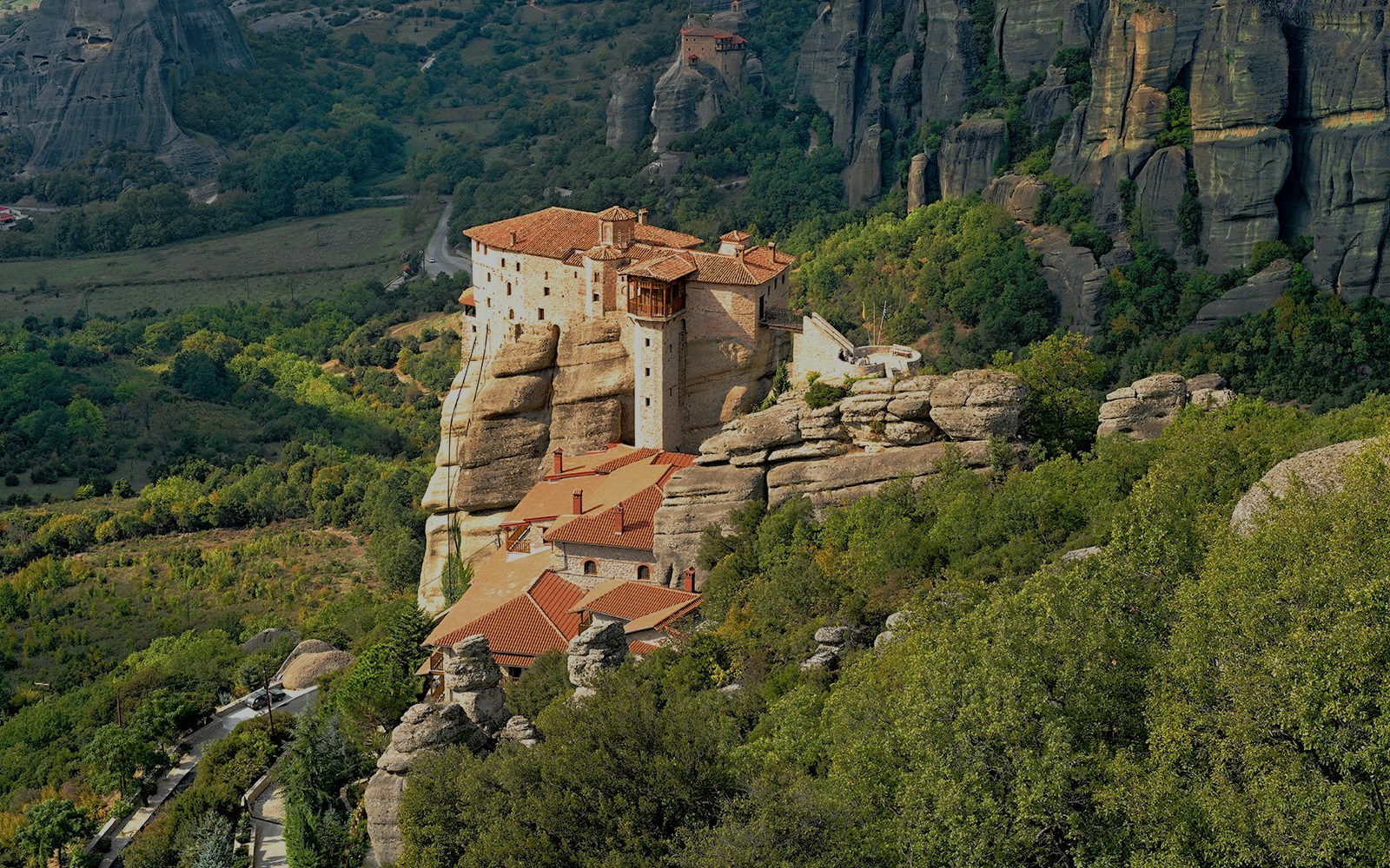 Meteora monastery perched on rock formations surrounded by lush greenery, Greece.