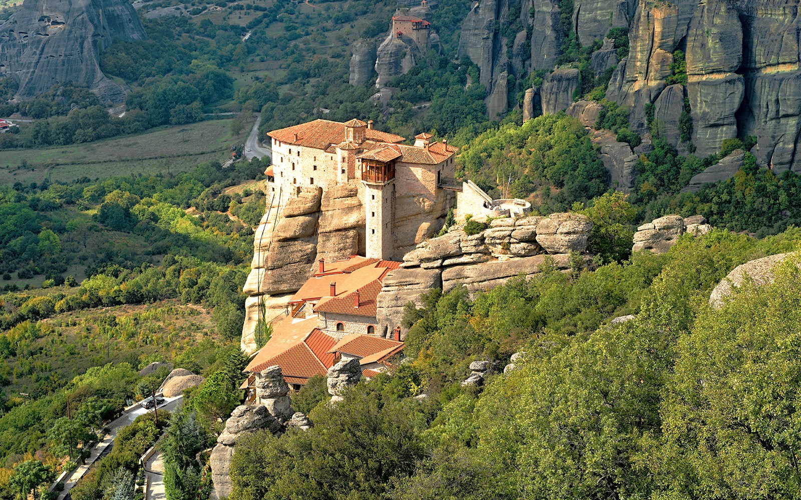 Meteora monastery perched on rock formations surrounded by lush greenery, Greece.