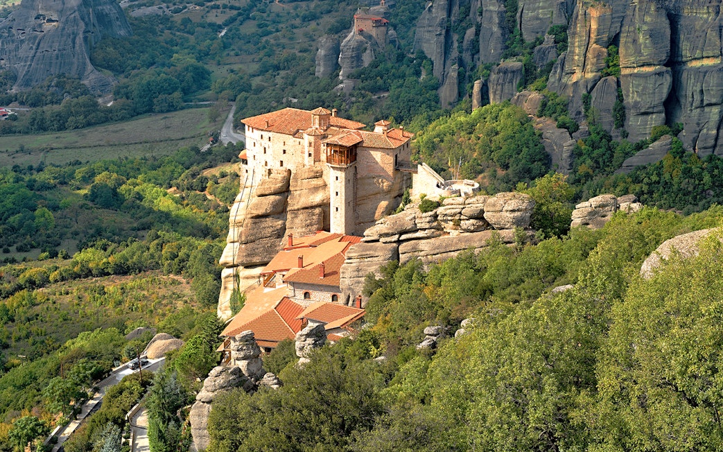 Meteora monastery perched on rock formations surrounded by lush greenery, Greece.