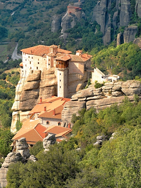 Meteora monastery perched on rock formations surrounded by lush greenery, Greece.