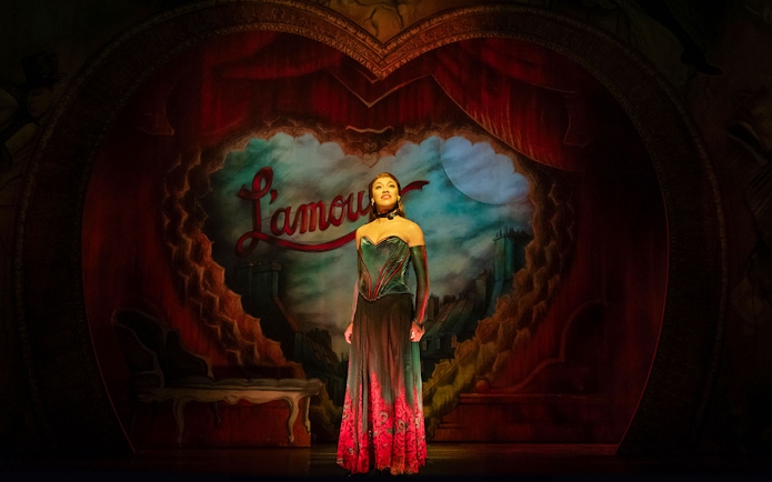 Performer on stage at Moulin Rouge! The Musical, West End, with Parisian backdrop.