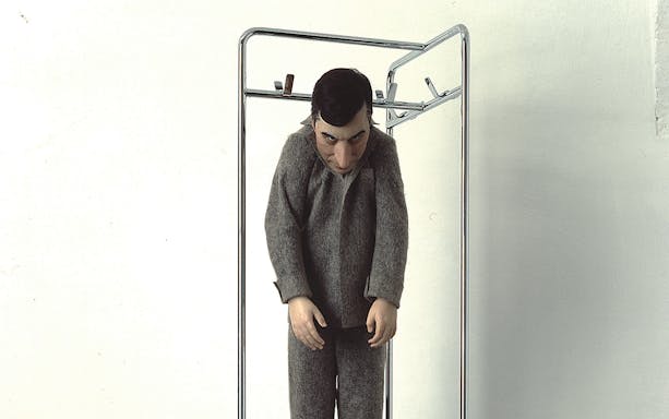 Sculpture of a man in a gray suit hanging from a metal frame.