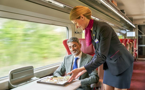 Crew serving meal to first class passenger on a train journey.