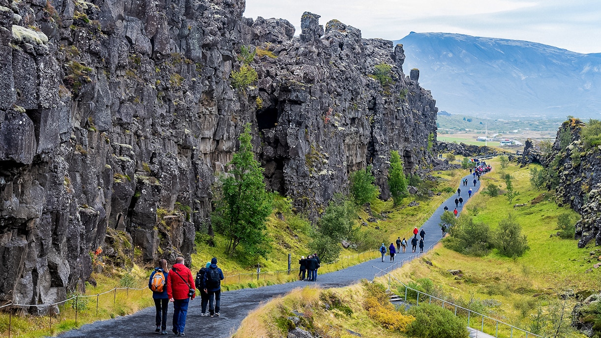 Visitors walking along a path between rocky cliffs in Þingvellir National Park, Iceland.