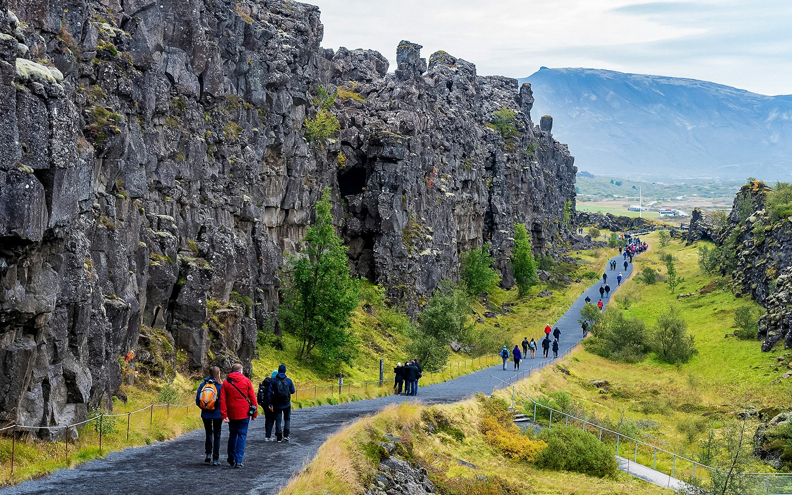 Visitors walking along a path between rocky cliffs in Þingvellir National Park, Iceland.