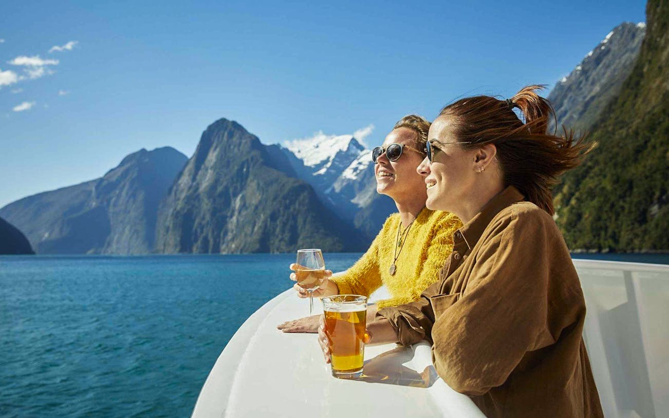 Cruise passengers enjoying drinks with views of Milford Sound fjords.