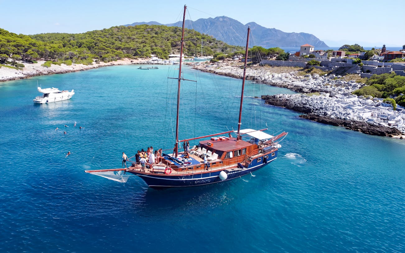 Sailing boat with tourists in Saronic Gulf near Athens, Greece, with swimmers in clear blue water.