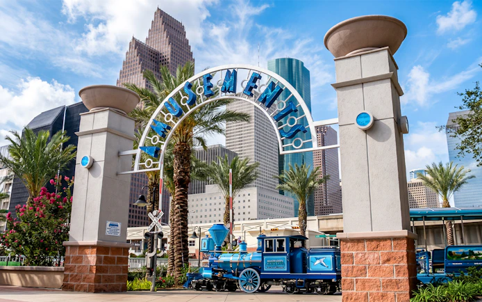 Downtown Aquarium Houston entrance with blue train and city skyline.